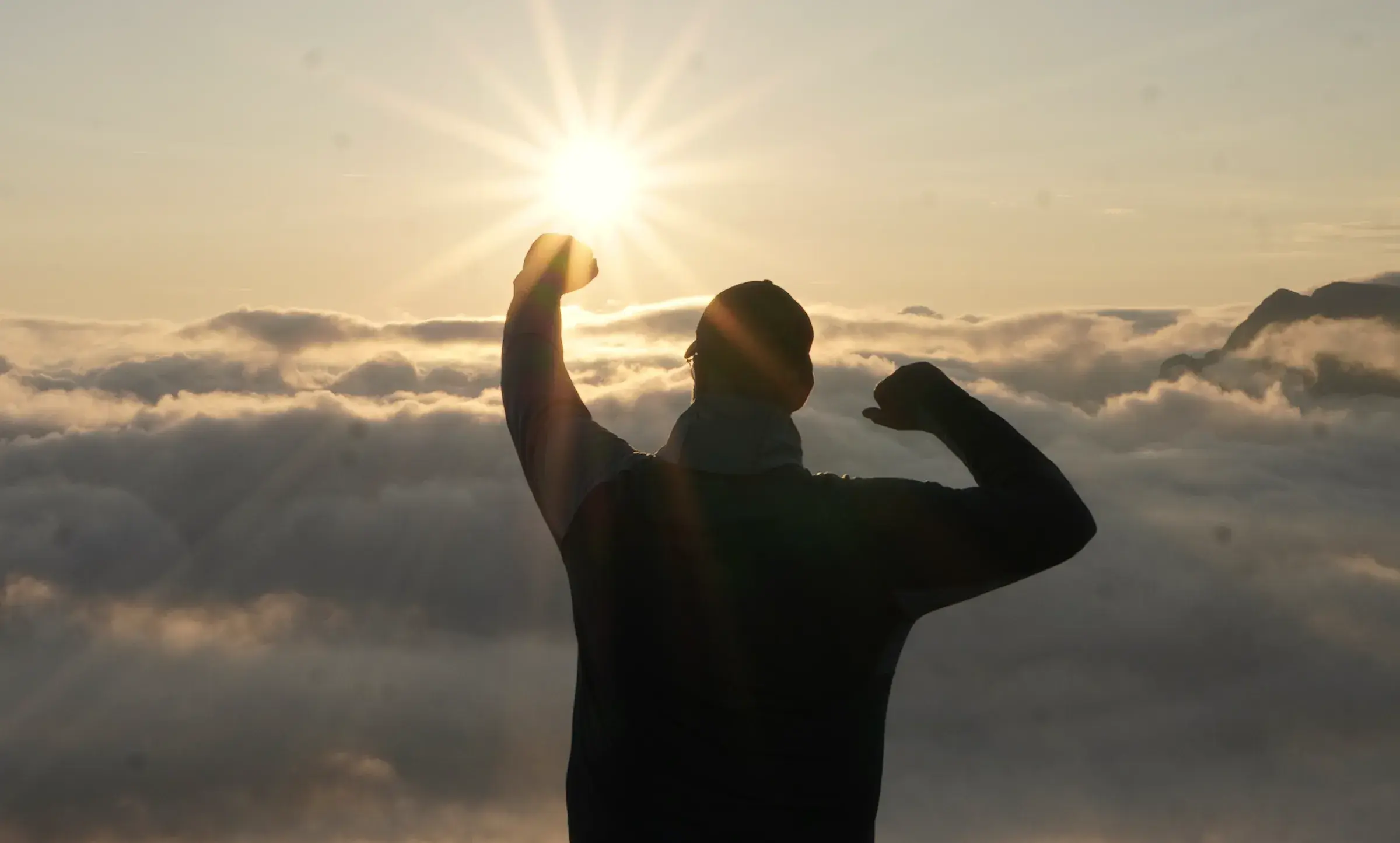 Silhouette von Andreas Hinz vor der aufgehenden Sonne über einem Wolkenmeer.