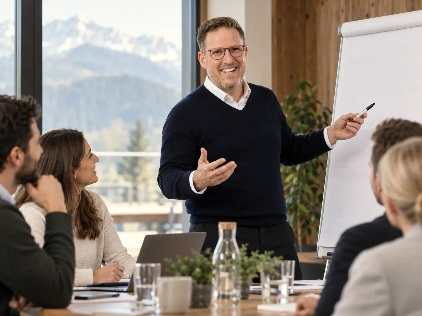 Andreas Hinz moderiert am Flipchart einen Workshop mit einem Führungsteam, im Fenster die Berge.