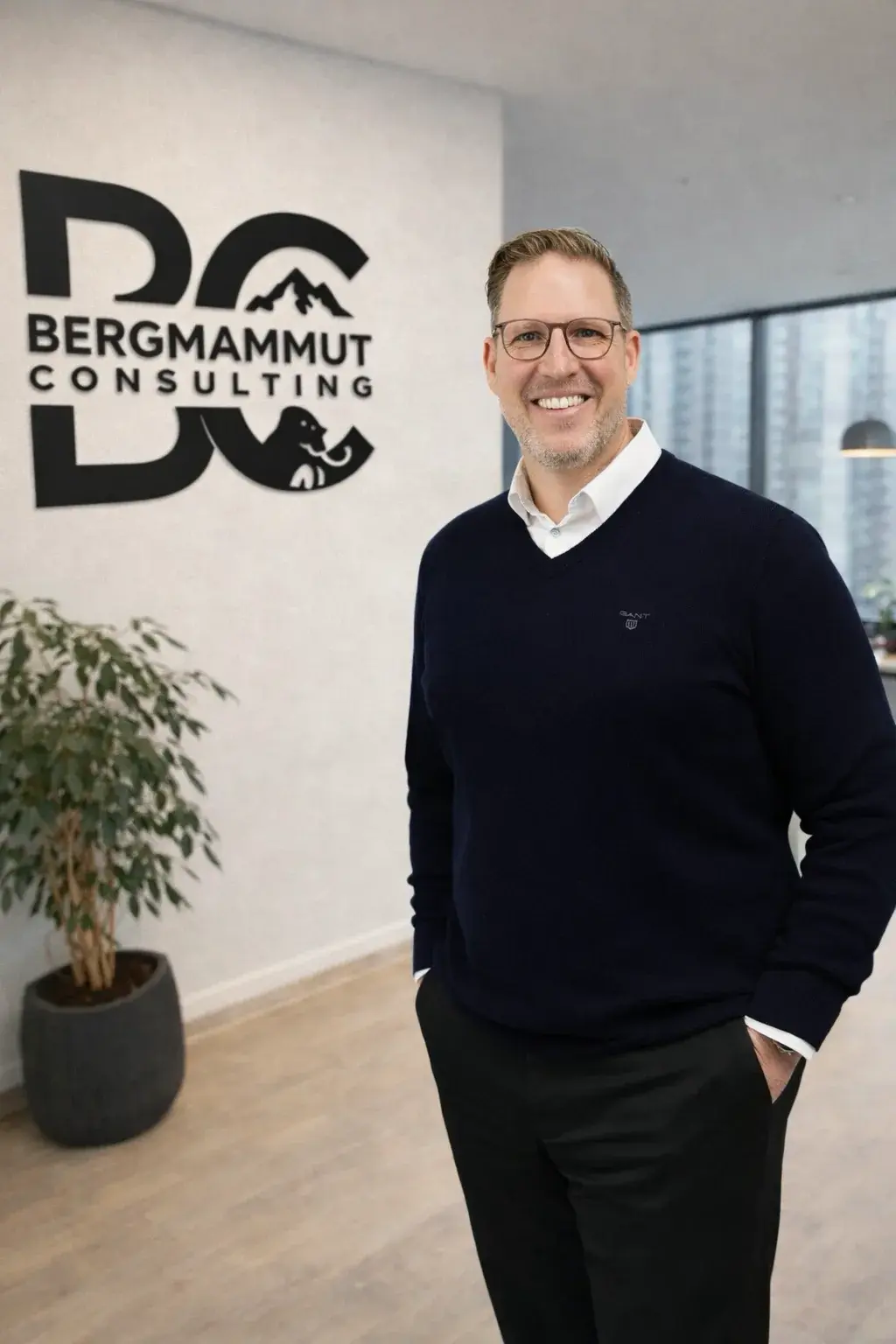 Andreas Hinz im Büro, im Hintergrund das Logo von Bergmammut Consulting an der Wand.